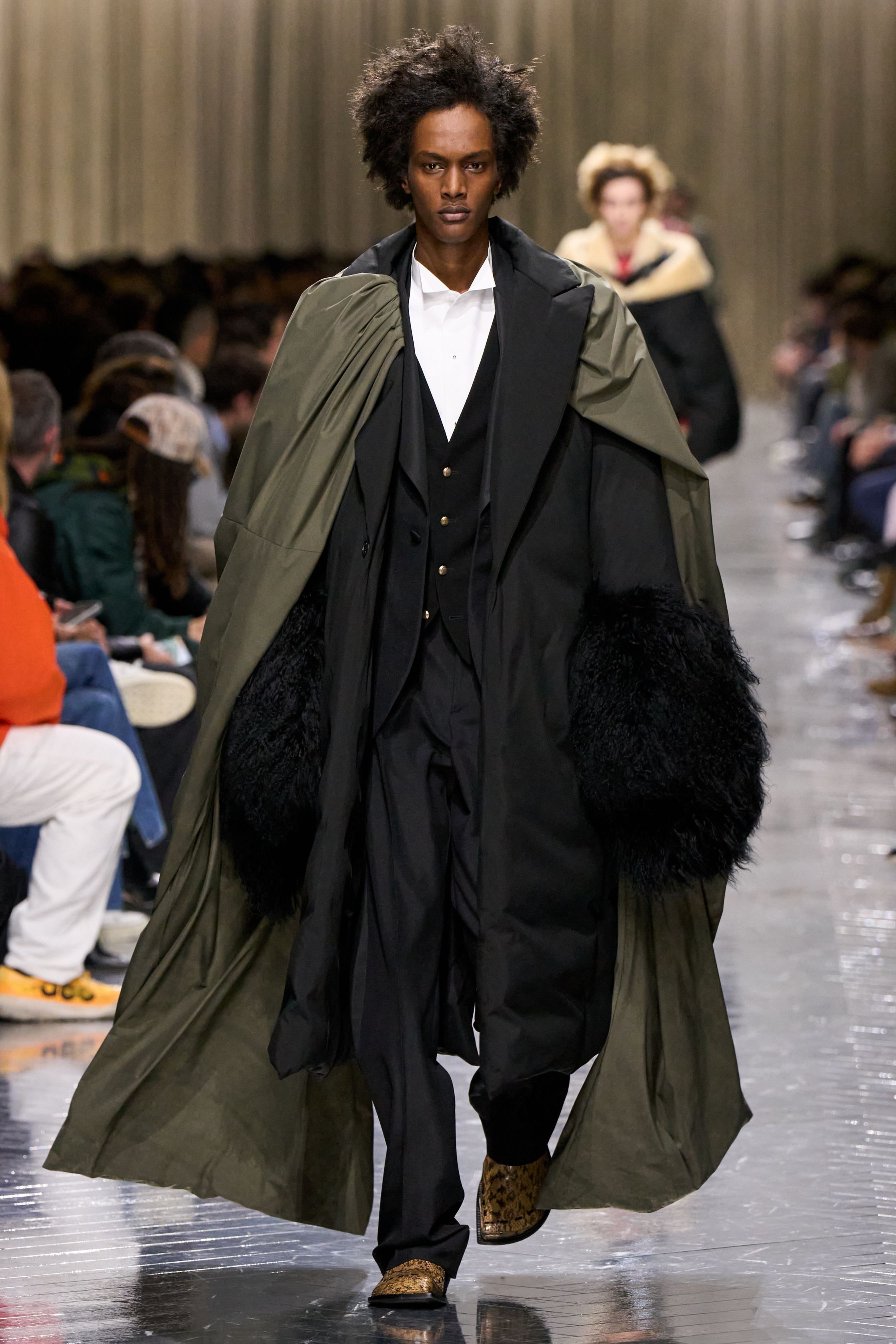 本季 Dior Men 2026 秋冬在克制与叛逆之间建立起新的男性气质坐标。轮廓上，柔软针织、披风式外套与军装结构形成张力对照，模糊正装与休闲、性别与功能的边界；材质层面，羊毛、皮革、毛绒与轻量技术面料并置，强化“触感叙事”。色彩从学院派的灰蓝、橄榄绿过渡至点状印花与手工肌理，传递一种被精心编排的随性。整体呈现出一种“新贵游牧者”形象：既有高级定制的工艺根基，又拥抱当代青年对自由、混搭与身份流动性的渴望-顽石频道趋势研究
